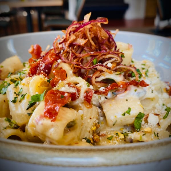 Close-up of creamy Italian pasta with crispy fried onions, sun-dried tomatoes, and fresh herbs.