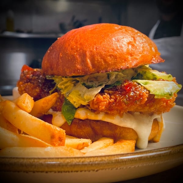 A crispy chicken burger with lettuce, sauce, and a side of golden fries on a plate.
