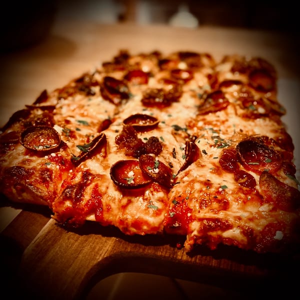 Close-up of a rectangular pepperoni pizza with melted cheese and herbs on a wooden board.