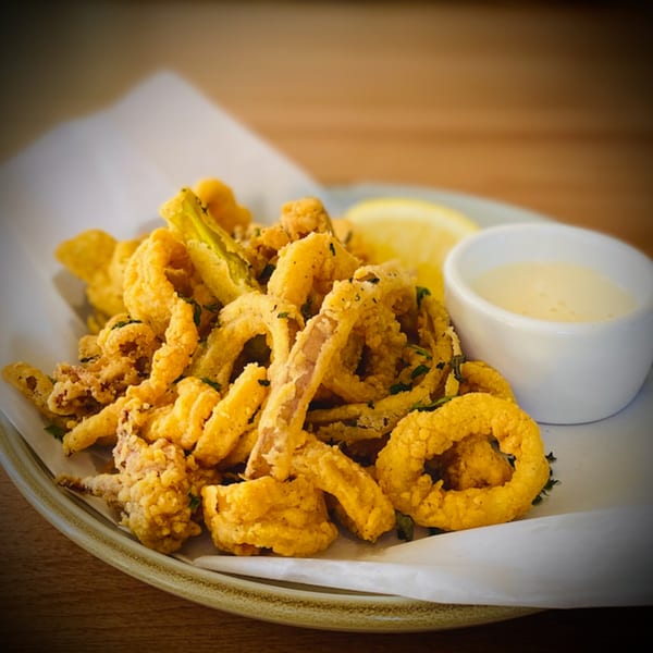 Crispy fried calamari and zucchini, with a lemon wedge and aioli, on a white plate.