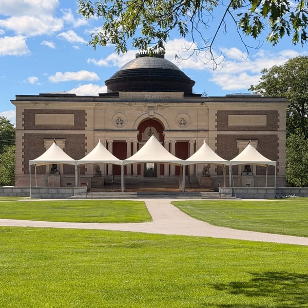 Five white tents line the front of the Walker Art Building, with a green lawn and blue sky.