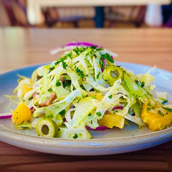 Close-up of a fresh Italian salad with shredded lettuce, oranges, olives, and red onion.