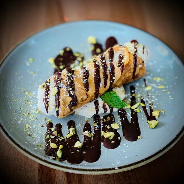 A Pomelia cannolo, drizzled with chocolate and pistachios, on a light blue plate.