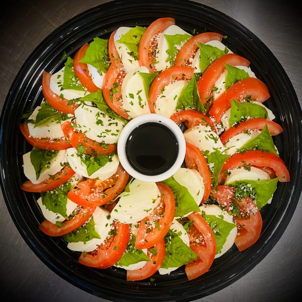 Pomelia's Caprese salad with sliced tomatoes, mozzarella, basil, and balsamic glaze on a black platter.