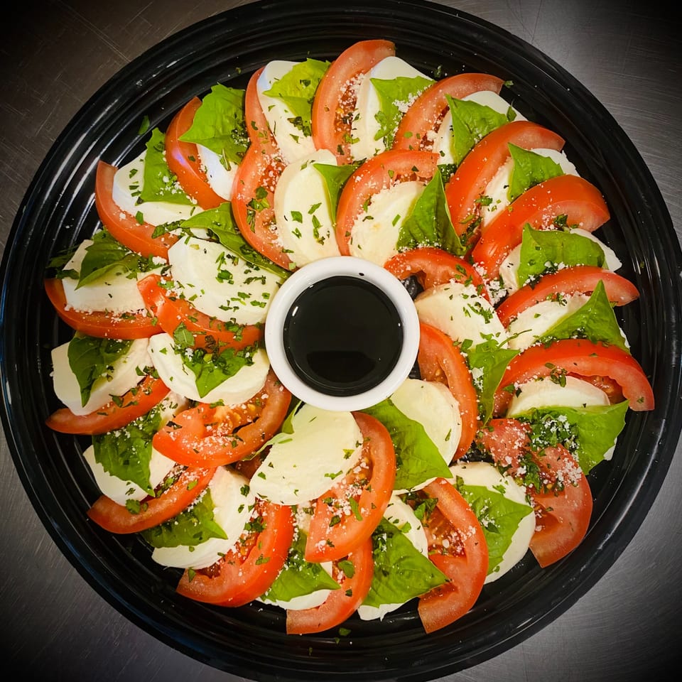 Pomelia's Caprese salad with sliced tomatoes, mozzarella, basil, and balsamic glaze on a black platter.